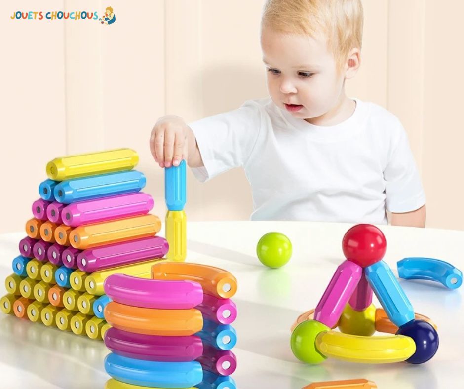 Un enfant empile des pièces colorées d'un jeu de construction magnétique sur une table blanche.