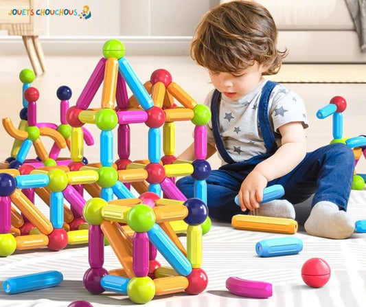 Un enfant joue avec un jeu de construction magnétique coloré, portant une salopette bleue et un t-shirt étoilé