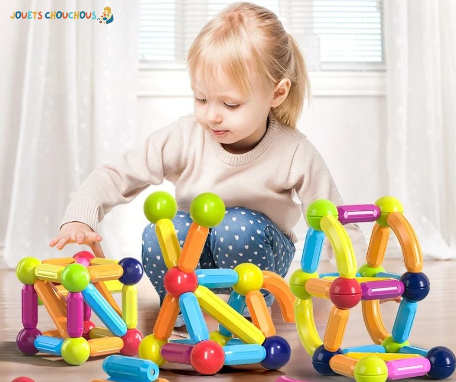 Petite fille assemble des structures colorées avec un jeu de construction magnétique sur le sol.